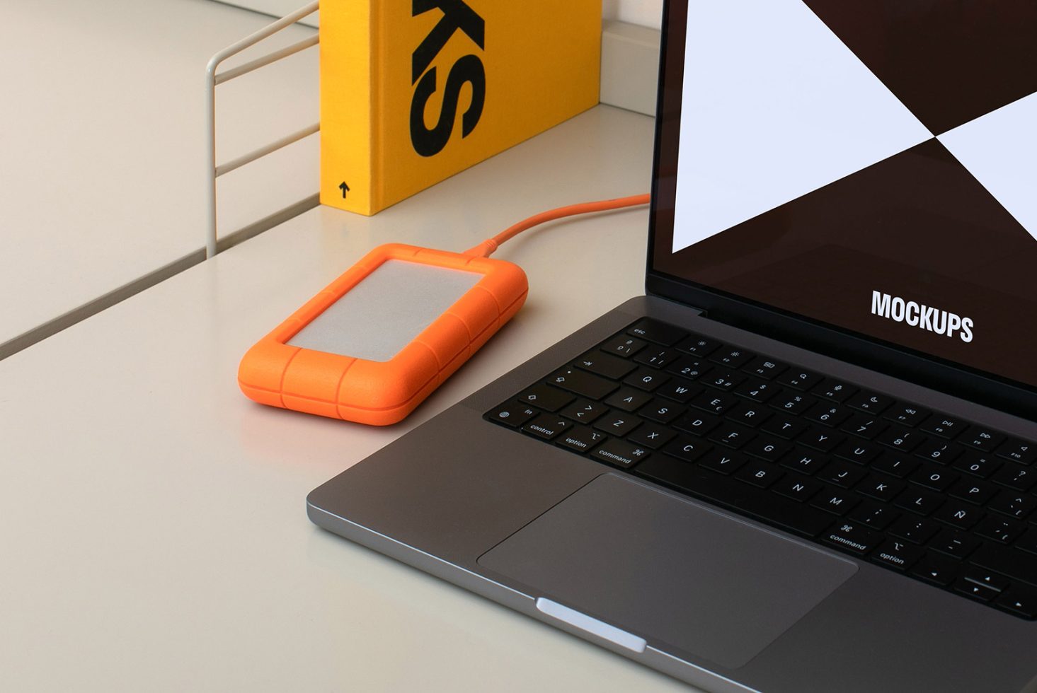 Laptop mockup with external orange hard drive for designers workspace. High-quality PSD mockup, ideal for showcasing web designs and digital assets.