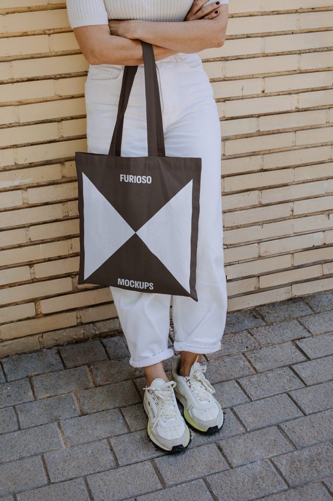 Person in white pants holding a Furioso mockup tote bag. Design showcases geometric graphics, ideal for designers searching for modern templates or stylish mockups.