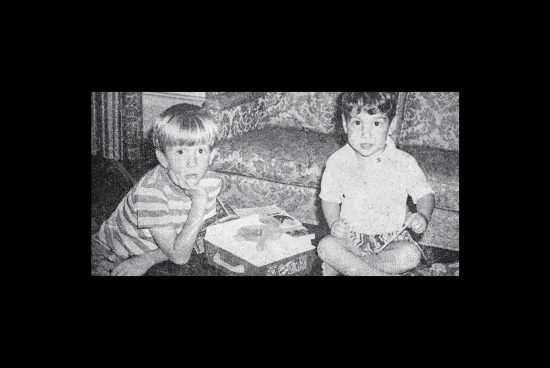 Vintage photo mockup of two boys sitting on a patterned couch, engaged in activity. Perfect for designers creating nostalgic or retro-themed graphic projects.