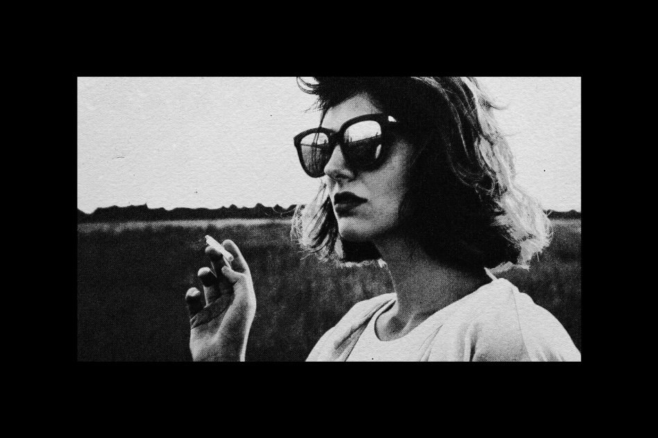 Black and white portrait of a woman in sunglasses holding a cigarette. Ideal for graphic design projects, posters, and retro-style templates. Moody aesthetic.