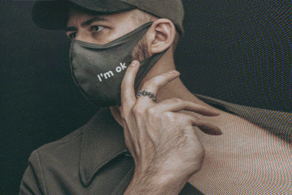 Man wearing a mask with text Im ok and a ring on his hand, dressed in a cap and jacket. Suitable for graphic designers creating COVID-19-related designs.