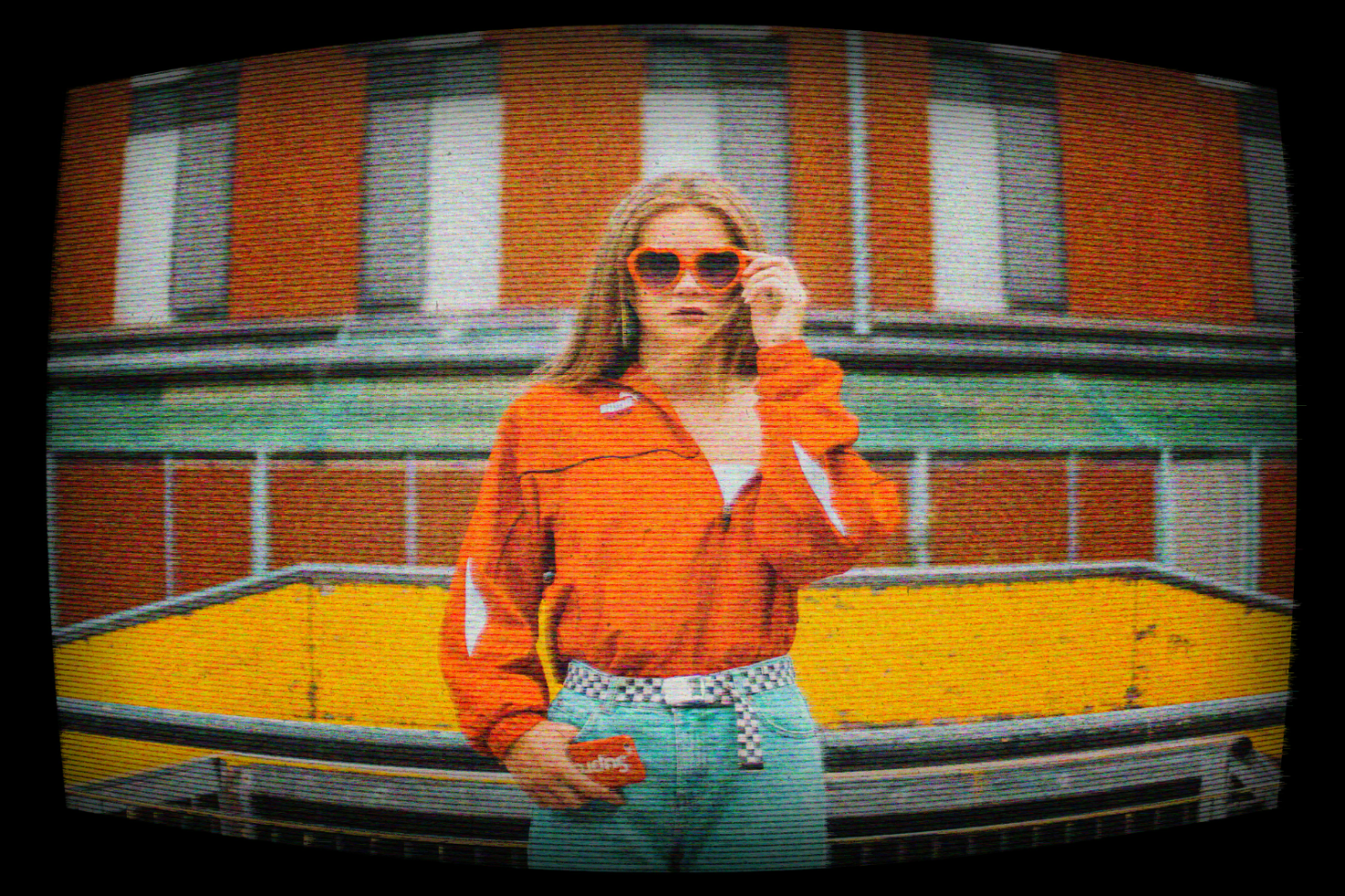 Vintage photo of a woman in retro attire wearing heart-shaped sunglasses and an orange jacket, with a building background. Suitable for graphic design templates.