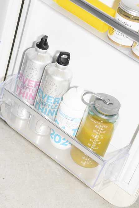 Refrigerator door shelf with stainless steel and plastic water bottles, glass juice container. Storage, kitchen, hydration, glass bottles, organization.