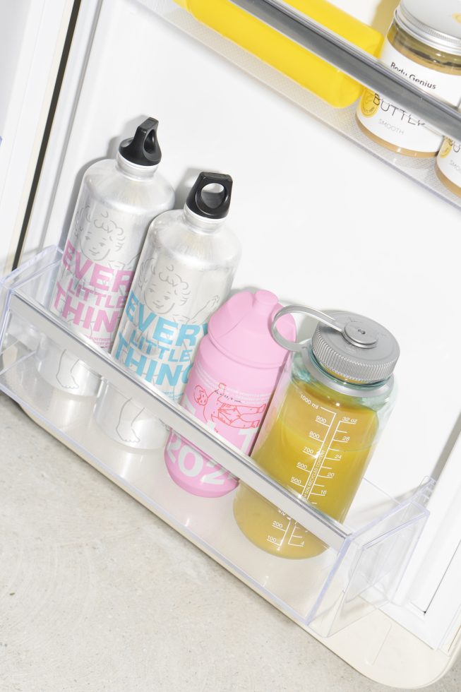 Water bottles and glass containers with liquid stored in a refrigerator door shelf. Kitchen storage mockup, fridge organization. Ideal for lifestyle design projects.