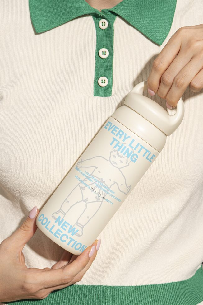 Person holding a beige water bottle with blue text and an illustration wearing a cream and green sweater. Keywords: product photography, accessory mockup, design template.