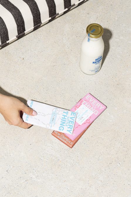 Hand holding designed food packaging, with a bottle of kefir and striped cushion in the background. Ideal for mockups, graphic design assets, designer resources.