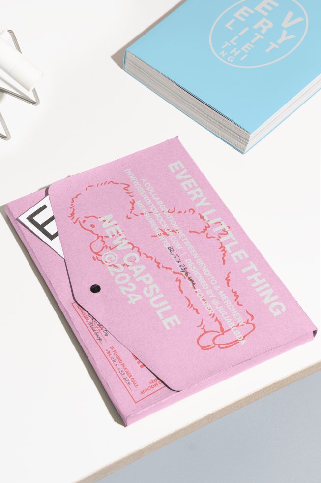 Flat lay of a pink envelope with text overlay on a white desk near a closed blue notebook. Ideal for designers. Mockup, stationery, branding, packaging.