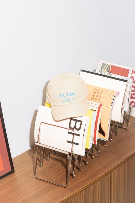 Magazine rack mockup with assorted books and beige cap on wooden table; minimalist workspace design; digital assets for mockups and templates.