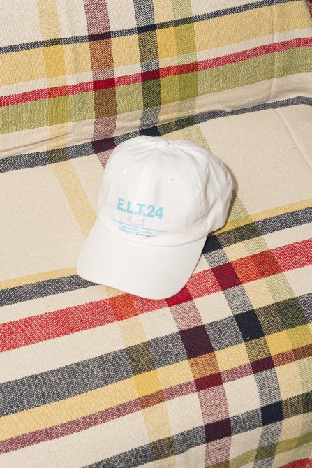 White cap with text ELT.24 displayed on a colorful checkered fabric background perfect for mockup template graphics use by designers on Marketplace.