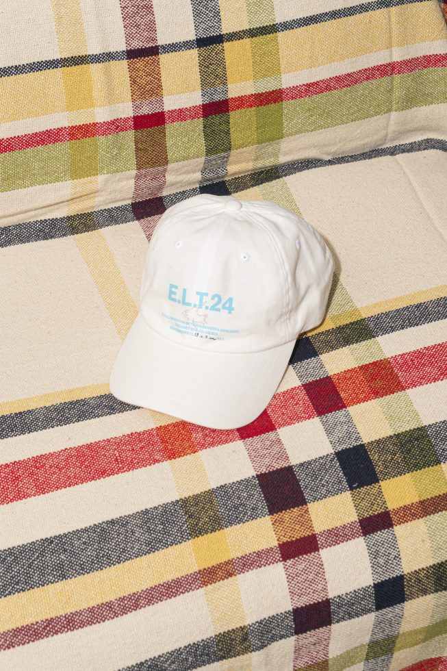 White cap with text ELT.24 displayed on a colorful checkered fabric background perfect for mockup template graphics use by designers on Marketplace.