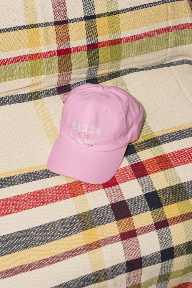 Pink baseball cap with ELT24 logo on plaid fabric background. Perfect for clothing mockups, apparel design and accessory templates. High quality graphic.