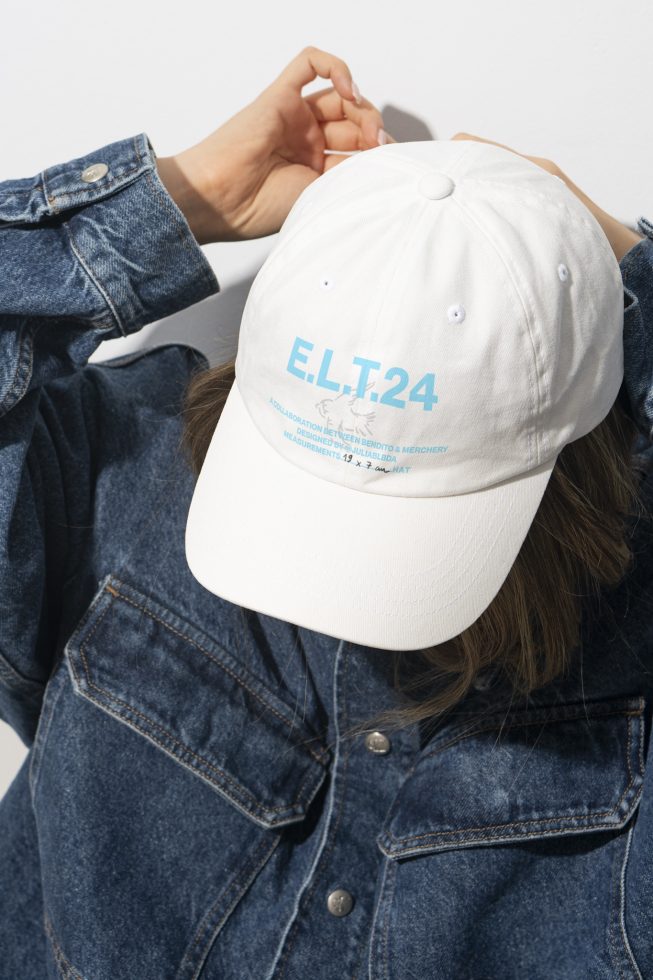 Close-up of a person wearing a white cap with blue text while adjusting it. The person is in a denim jacket. Ideal for mockups and graphic design projects.