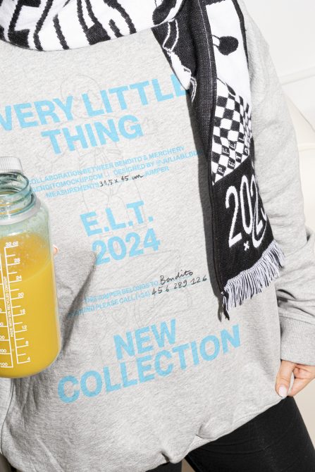 Mockup of a person wearing a gray sweater with blue text and holding a juice bottle designers digital assets new collection E.L.T 2024 fashion graphics templates