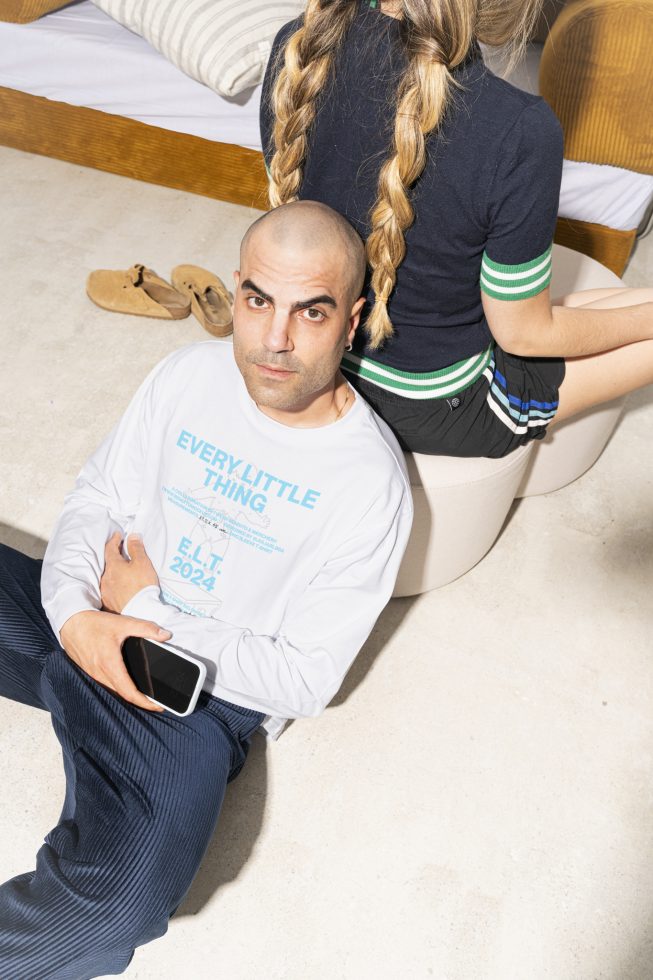 Man in branded T-shirt holding a phone next to a person with braided hair. Ideal for lifestyle mockups or clothing templates in graphic design projects.