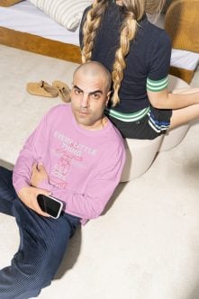 Overhead shot of guy in pink crewneck holding phone, woman standing behind with braids