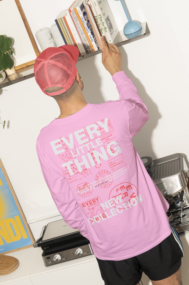 A person with a pink printed shirt and red mesh cap organizing books on a shelf in a modern kitchen. Keywords: mockup, shirt, cap, modern, kitchen, print.