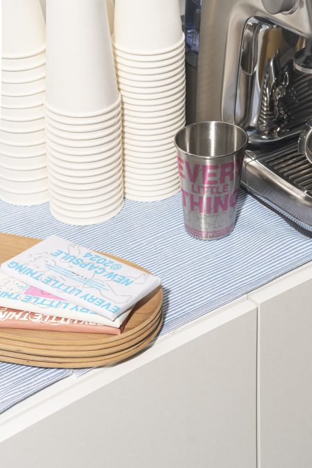 Photo of a kitchen counter with stacked disposable cups, a stainless steel cup, an espresso machine, a cloth, and a wooden tray. Perfect for mockups, graphics.