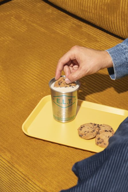 Hand dipping cookie into container on yellow tray over mustard fabric