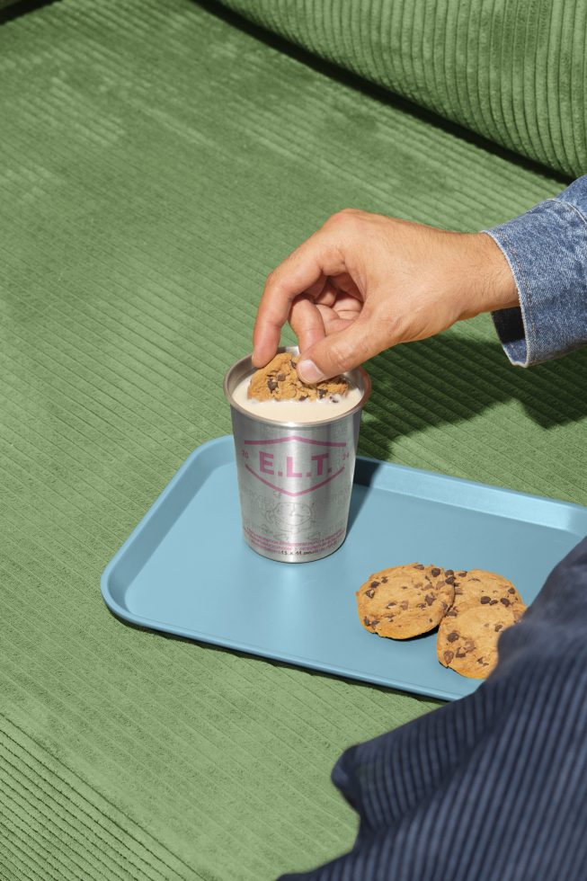 Hand dipping cookie in milk, green background, blue tray with cookies, denim sleeve visible. Ideal for mockups, design templates, creative graphics designers