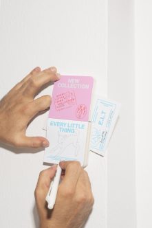 Hands holding pink, white, plus light blue book mockups from flat lay