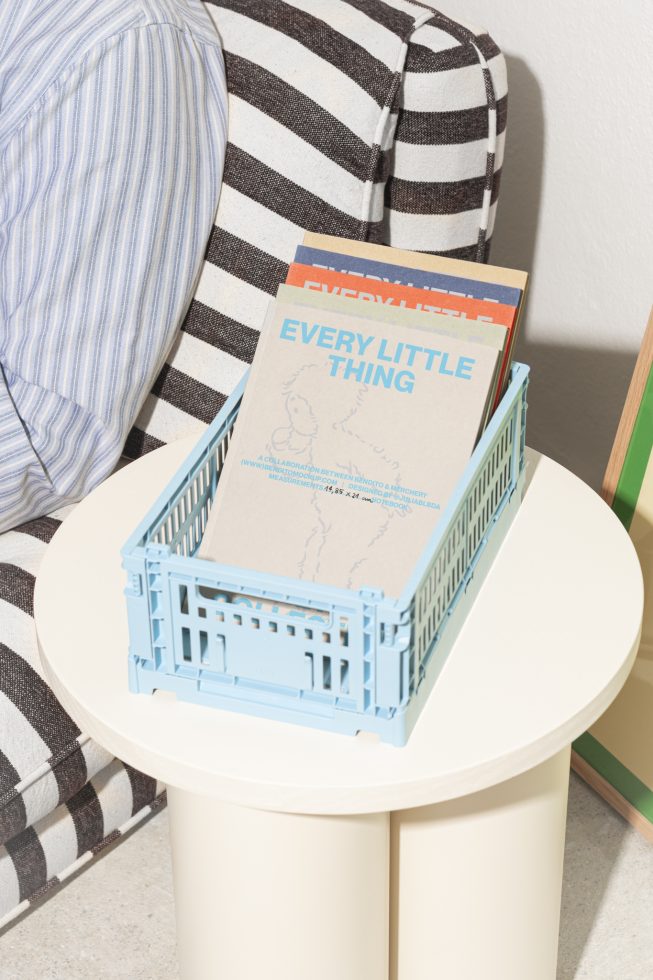 Cozy living room scene featuring blue crate of magazines on round table next to striped chair. Ideal for mockups, interior design, home decor enthusiasts.