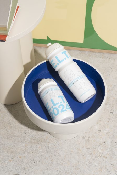 Mockup of two white customized water bottles with light blue text resting in a round white tray, suitable for graphic and template design projects.