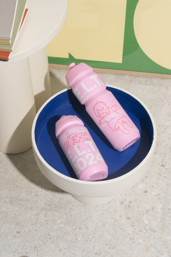 Two pink water bottles with minimalist designs featuring text and illustrations placed inside a blue and white bowl on a light stone surface.