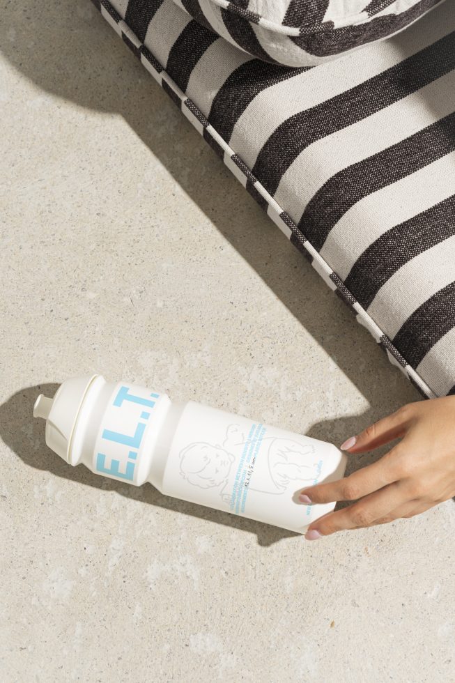 Bottle mockup in hand on concrete next to a striped cushion. Versatile, high-resolution background for designers on digital asset marketplace for Mockups, Graphics.