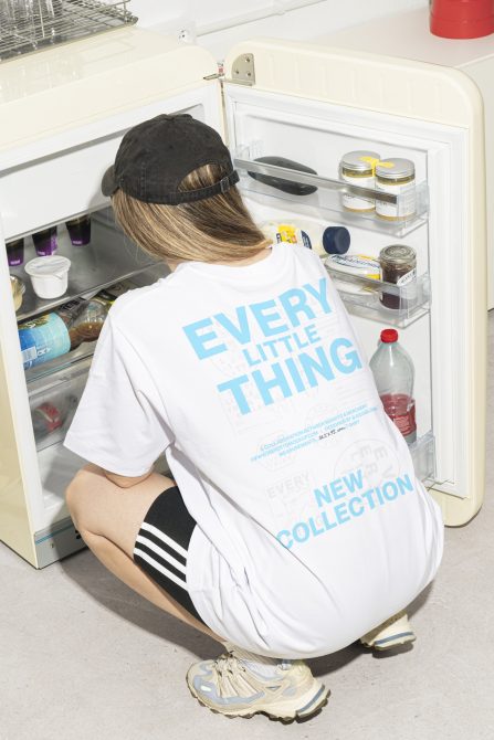 Person in casual outfit crouching in front of an open vintage refrigerator full of food items. Ideal for mockups, lifestyle branding, apparel design SEO