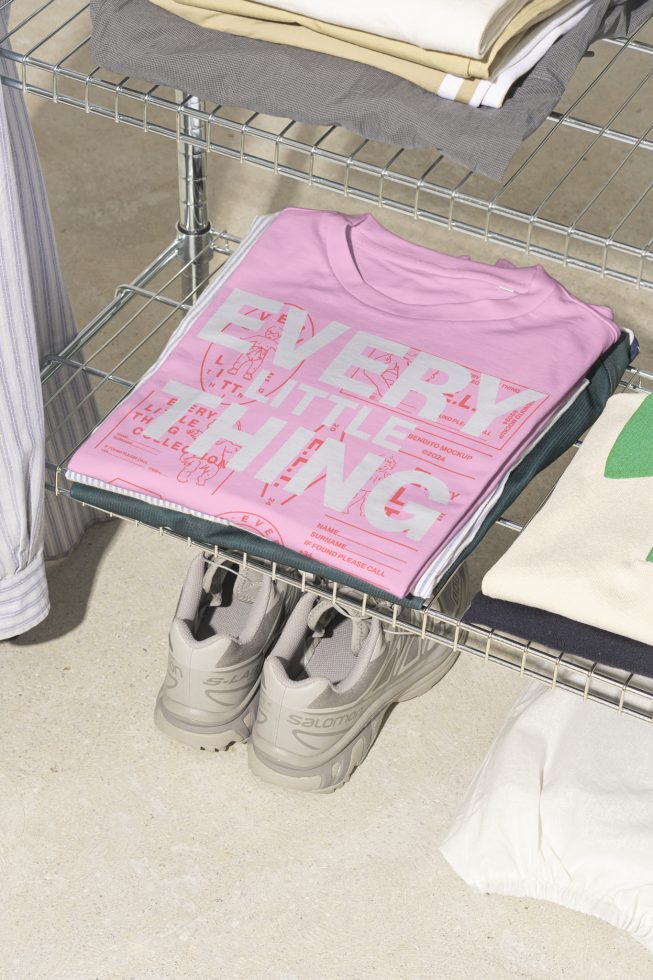 Styled mockup featuring folded pink graphic t-shirt on wire shelf next to sneakers and neatly stacked clothing suitable for designers and marketplace.