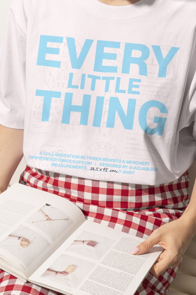 Close-up of person wearing a white t-shirt with blue text and holding a magazine, graphic design mockup, apparel template, design resource for designers.