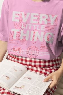 Oversized pink tee with red line art graphic, red gingham pants holding magazine laying down