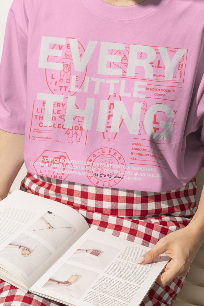 Person wearing a pink t-shirt featuring the text Every Little Thing holding an open magazine. Ideal for mockups and template designs for t-shirt projects