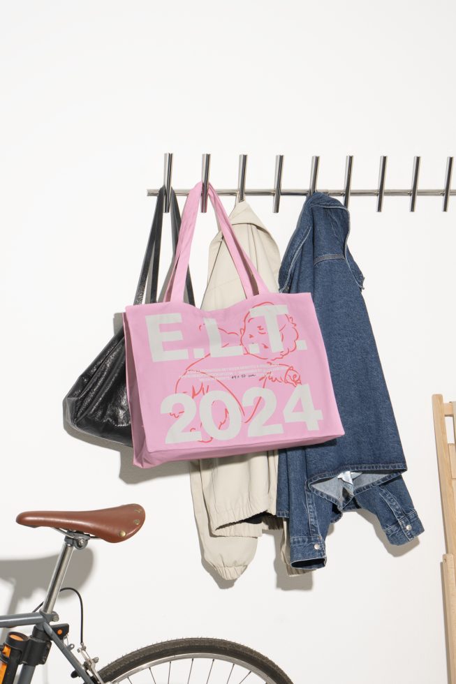 Tote bag mockup with 2024 text hanging on a coat rack next to a bicycle. Ideal for designers looking for trendy and practical tote bag templates for their projects.