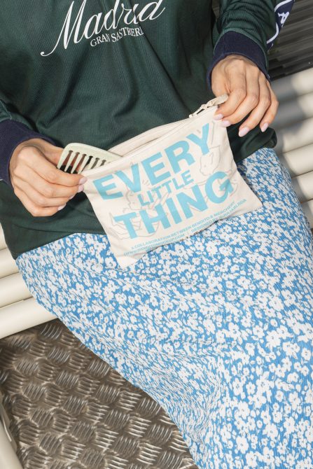 Hands opening cream canvas pouch with blue text, blue patterned fabric in background