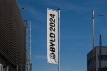 Vertical banner mockup hanging between industrial buildings with copyright symbol on white fabric against blue sky