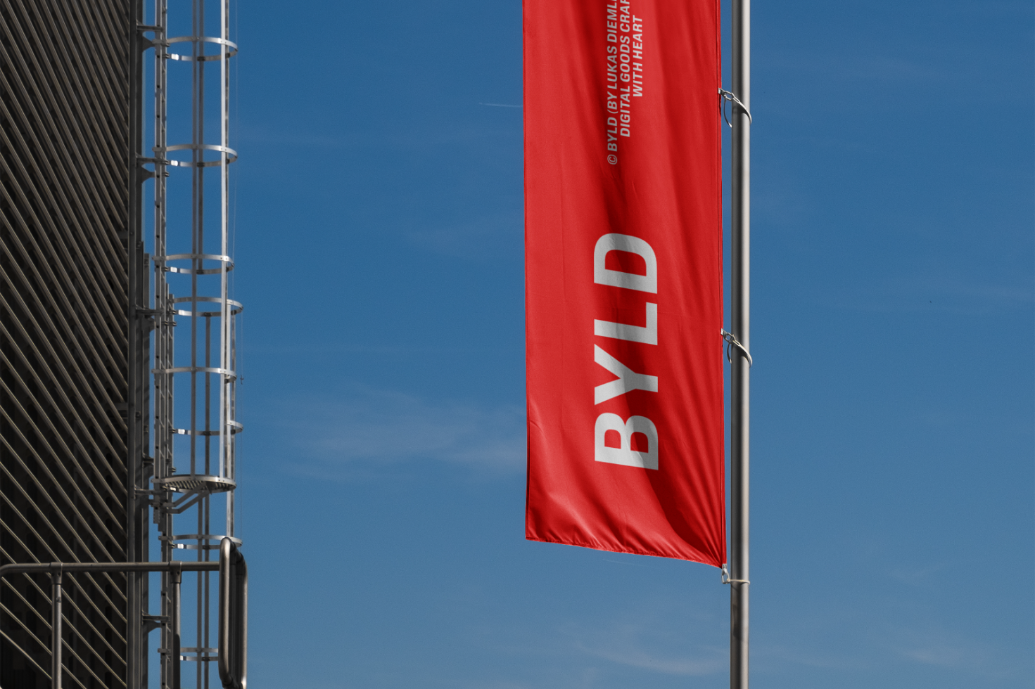 Red flag banner on corporate building facade displaying BYLD text with blue sky background. Ideal for mockups, advertising graphics, or brand templates.