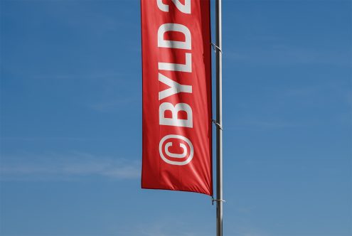 Red flag banner mockup with BYLD 2023 text against clear blue sky. Ideal for branding, signage, outdoor advertising. High-resolution template for designers.