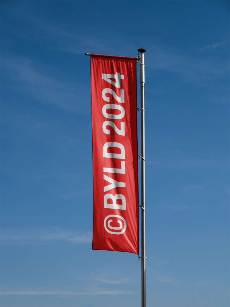 Vertical flag mockup with clear blue sky, red banner displaying BYLD 2024 in white text. Perfect for outdoor advertising templates and graphic design projects.