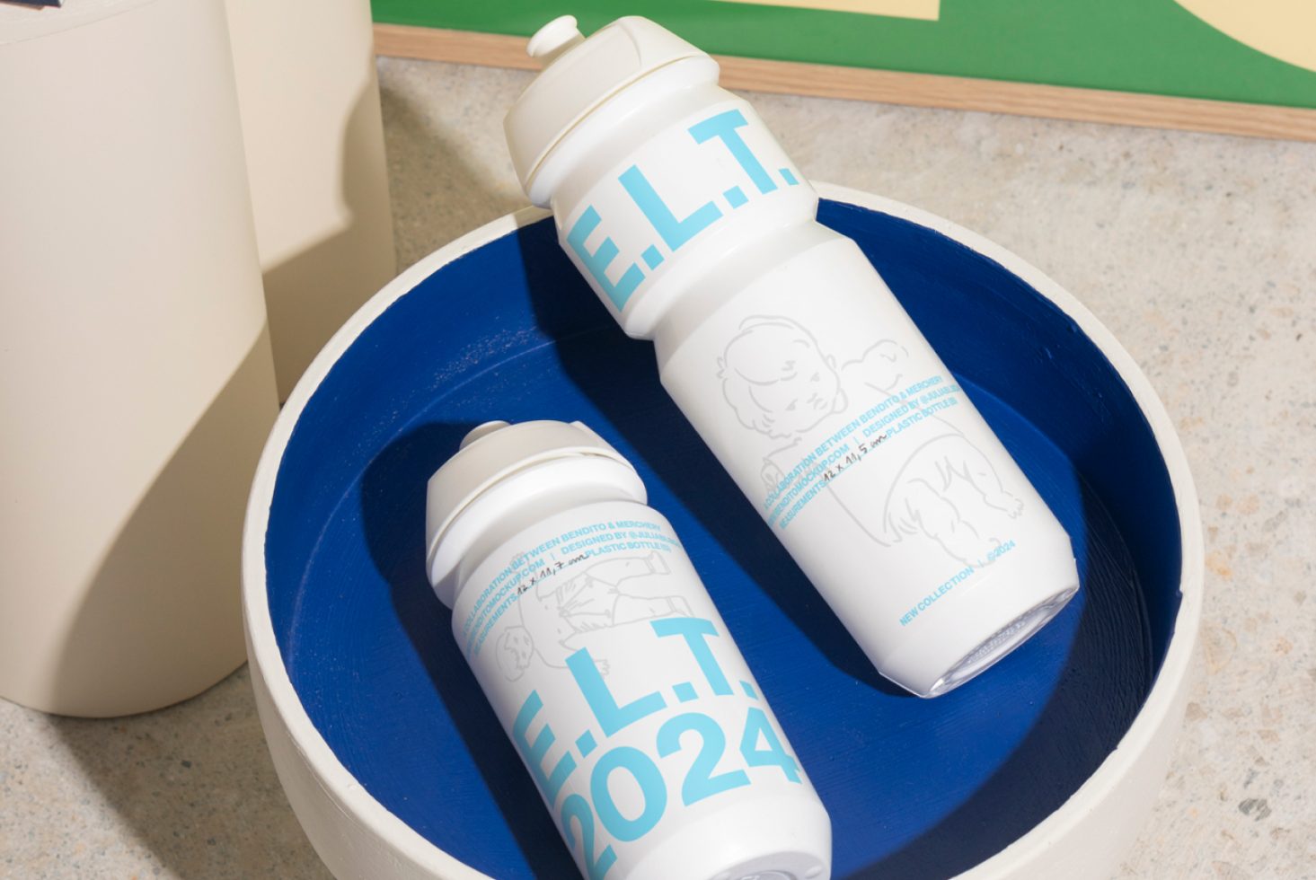 Two white water bottles with a blue logo in a blue bowl on a concrete surface. Perfect for mockups, product presentations, or branding projects for designers.