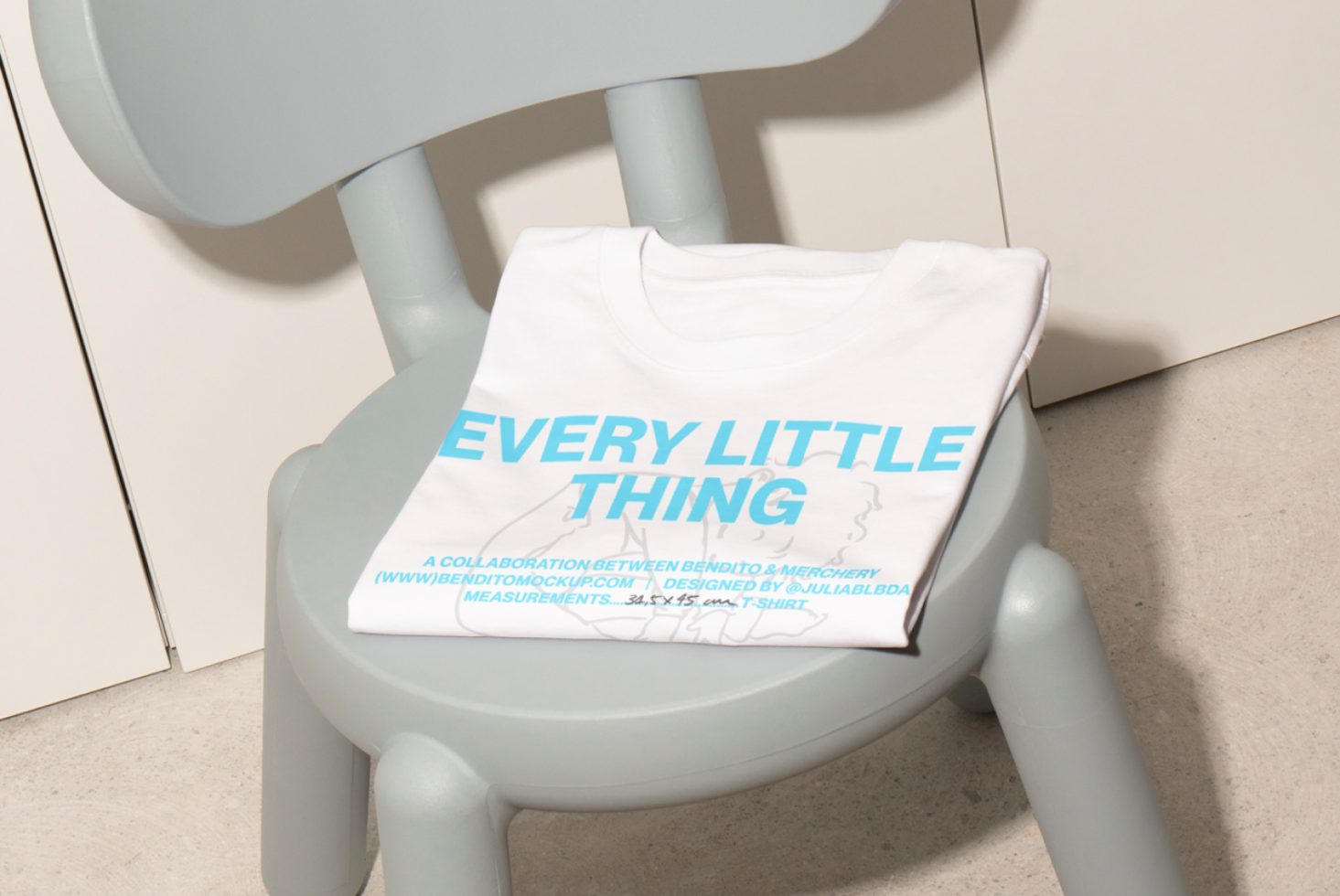 Folded white T-shirt featuring blue text reading Every Little Thing displayed on a grey chair ideal for apparel mockups and product presentations for designers