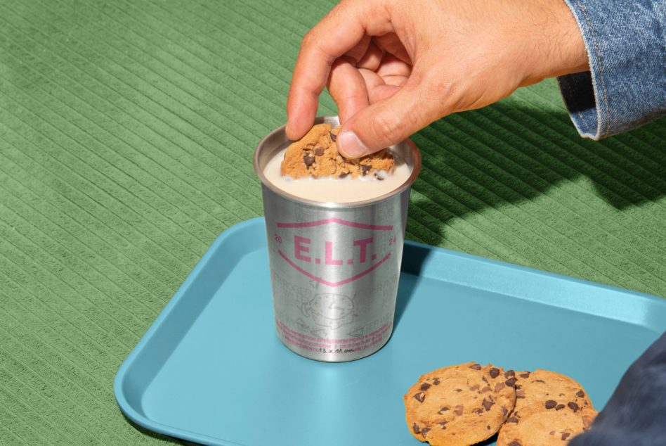 Hand dipping chocolate chip cookie into creamy drink in metallic can on blue tray