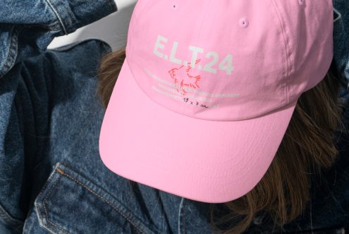 Close-up of a pink baseball cap with E.LT24 text and a graphic design worn by a person in a denim jacket casual fashion mockup design template accessory.