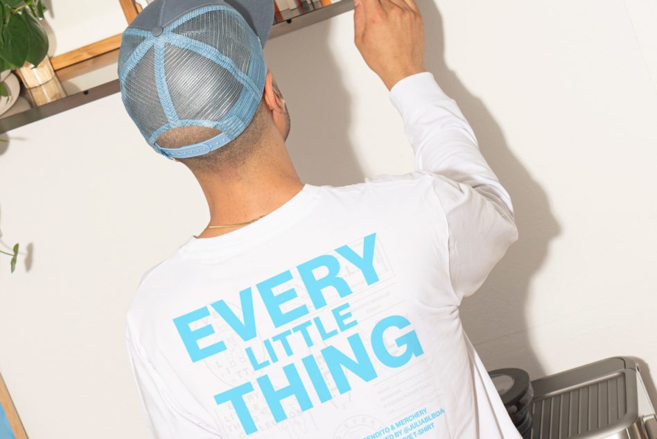 Close-up of white long-sleeve tee with blue typography, blue mesh cap visible