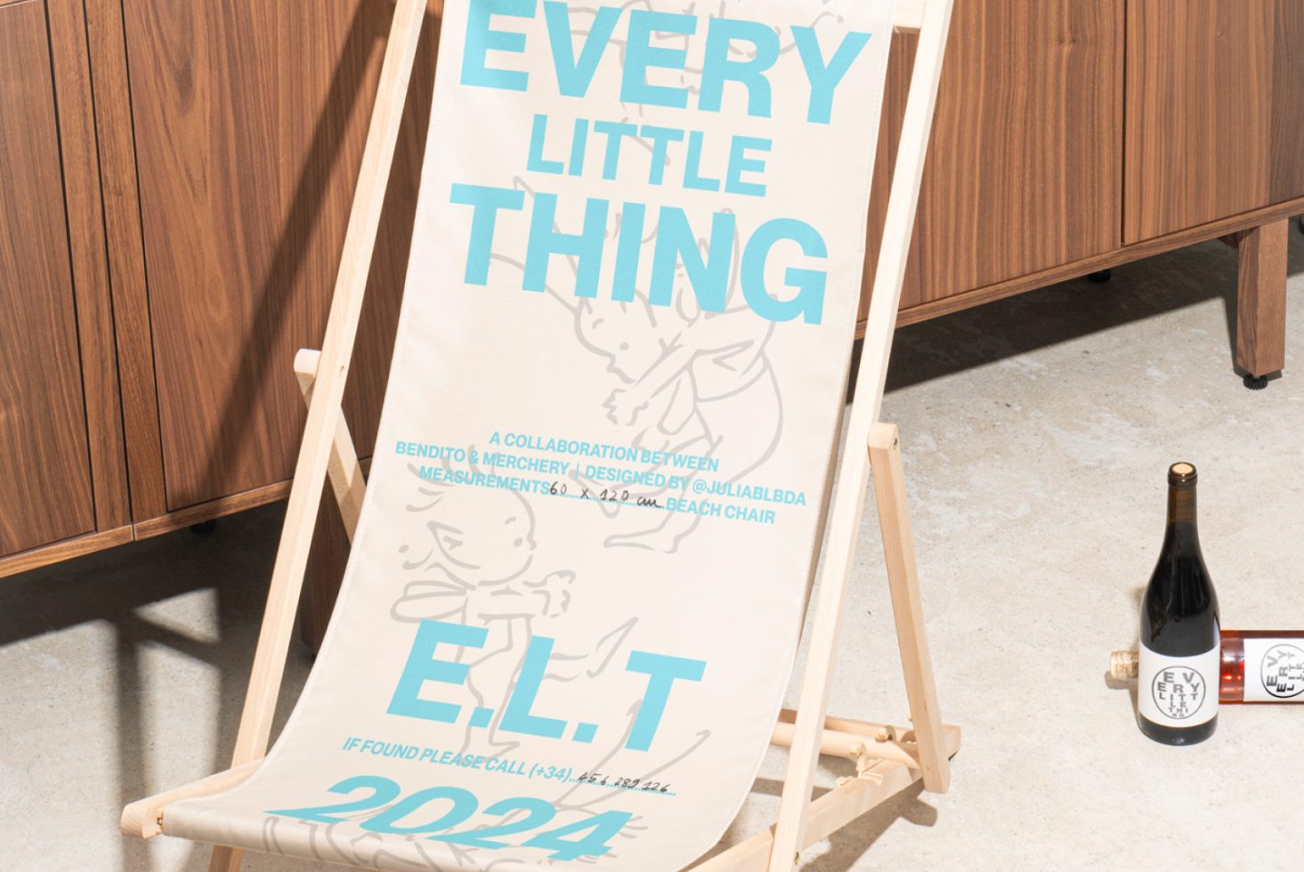 Beach chair mockup with text Every Little Thing in blue, leaning against a wooden cabinet. Ideal for graphic design, mockups, and templates for designers.