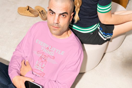 Man in pink long-sleeve shirt with Every Little Thing print sitting on floor next to a woman in black shorts, showcasing casual fashion design for templates and mockups.