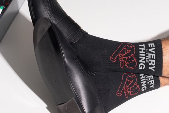 Close-up of black socks featuring graphic text Every Little Thing paired with black dress shoes. Ideal mockup for fashion and accessories designers to showcase work.