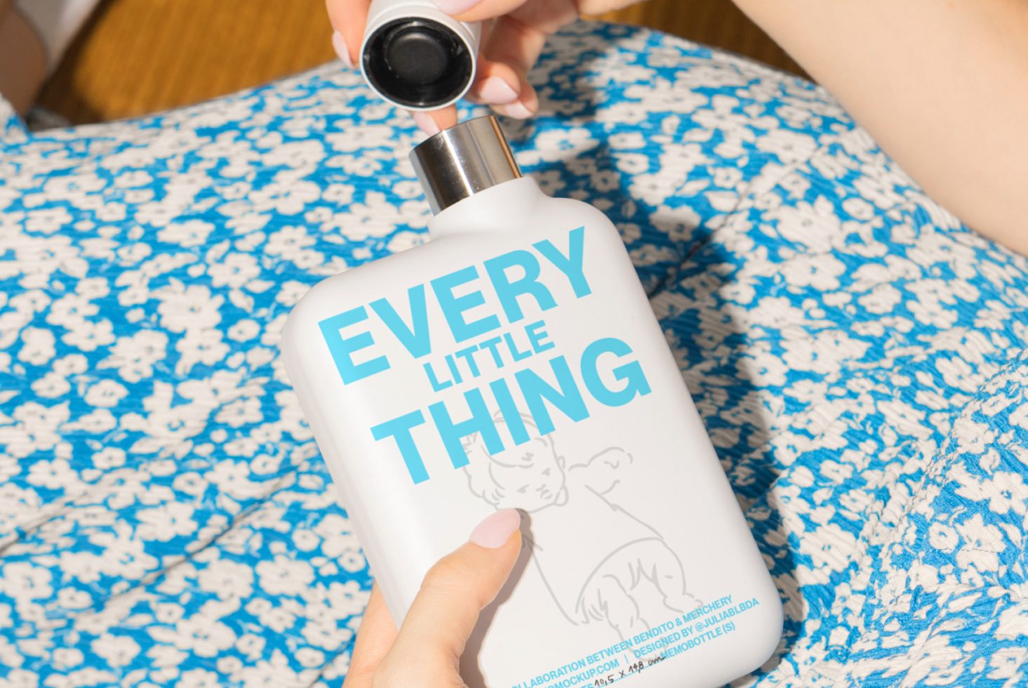 Hand holding a white water bottle labeled Every Little Thing on a blue floral background suitable for mockups and graphics for designers marketplace SEO keywords