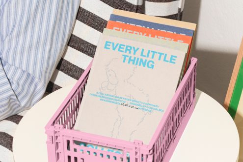 Stack of colorful notebooks in a pink crate on a striped fabric background. Mockup suitable for showcasing book cover designs. Keywords: mockup, notebooks, design template.