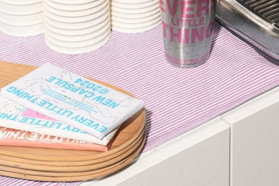 Folded t-shirts on wooden tray next to silver tumbler and stacked plates set on pastel striped tablecloth perfect for product mockups templates clothing branding